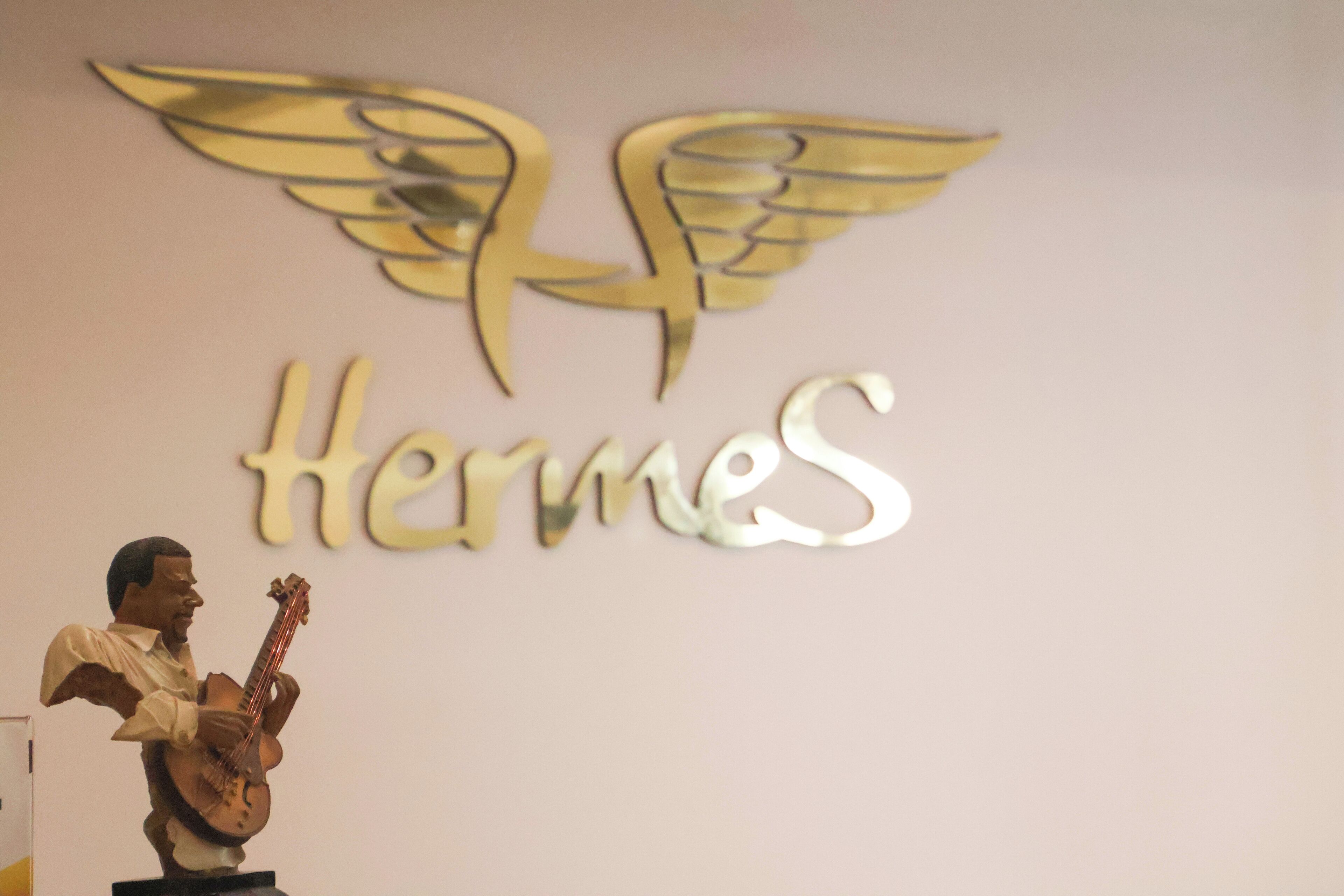 A statue of a man playing a guitar, a logo with wings, and the word "Hermes" on a wall.