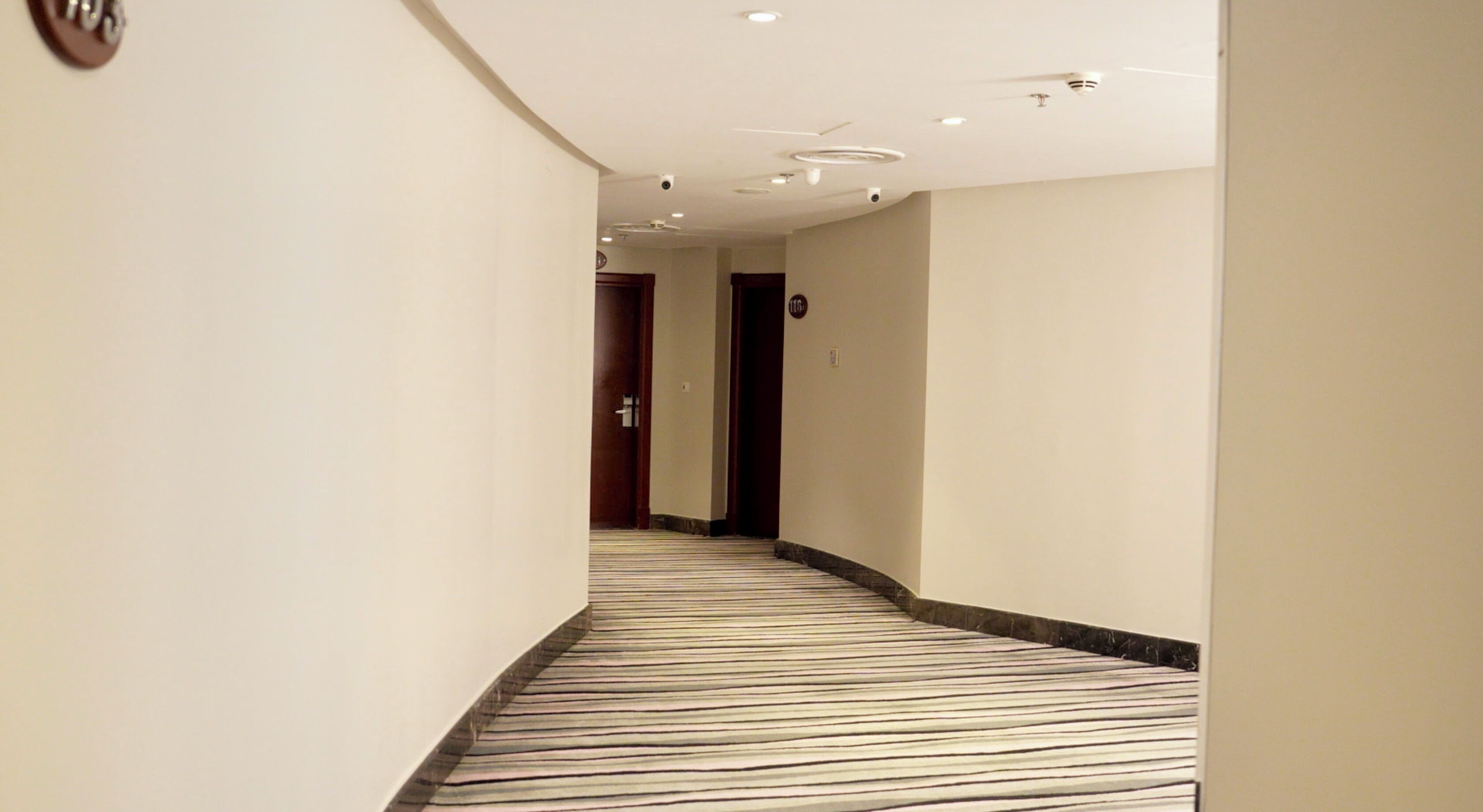 A hotel hallway with a striped carpet, a wooden door, and a ceiling with recessed lighting.