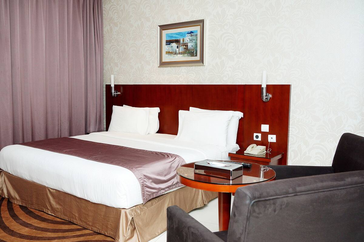 A hotel room with a large bed, a round table, a chair, and a painting on the wall.