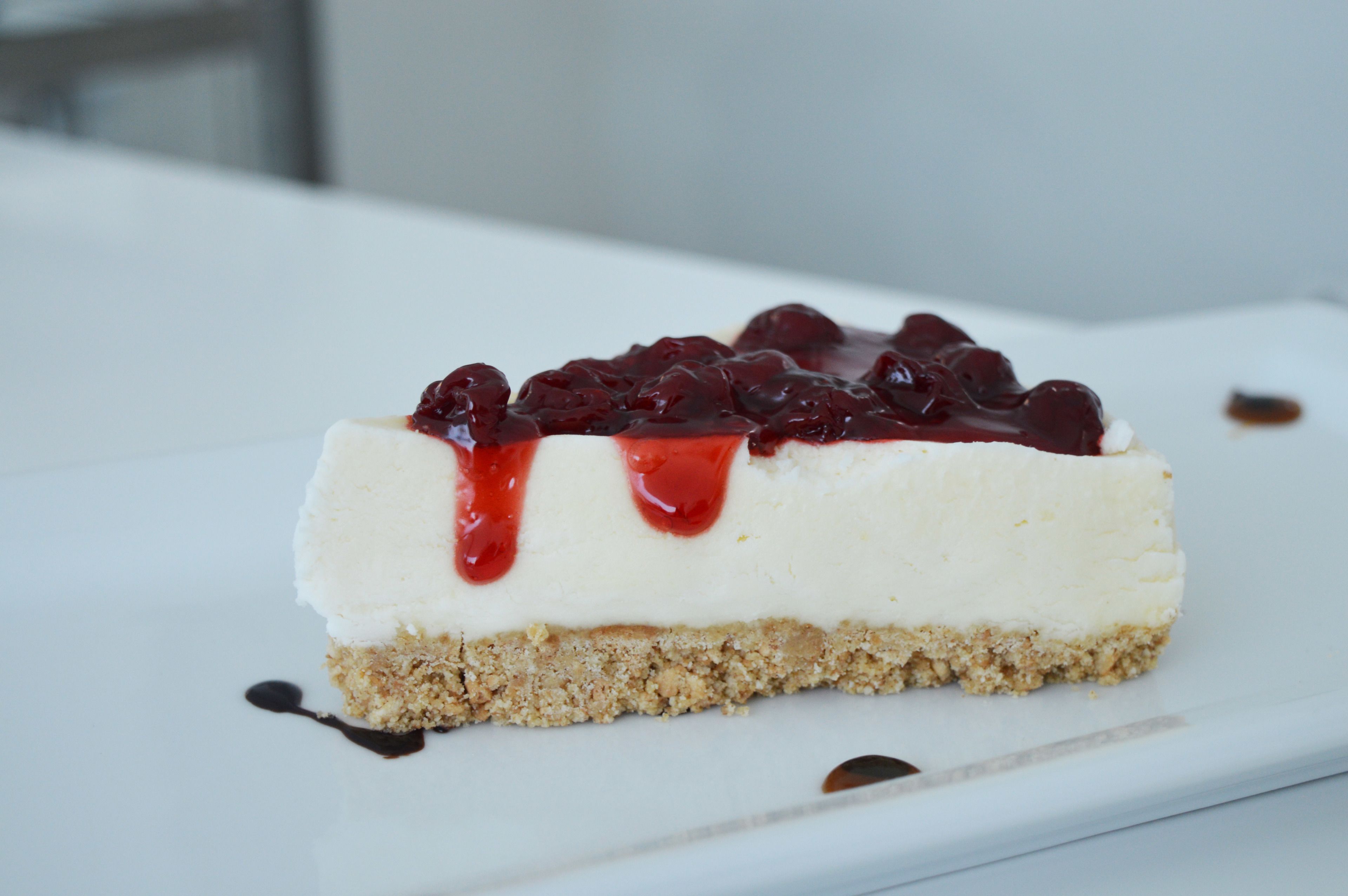 A slice of cheesecake with a berry topping and a crumbly base on a white plate.