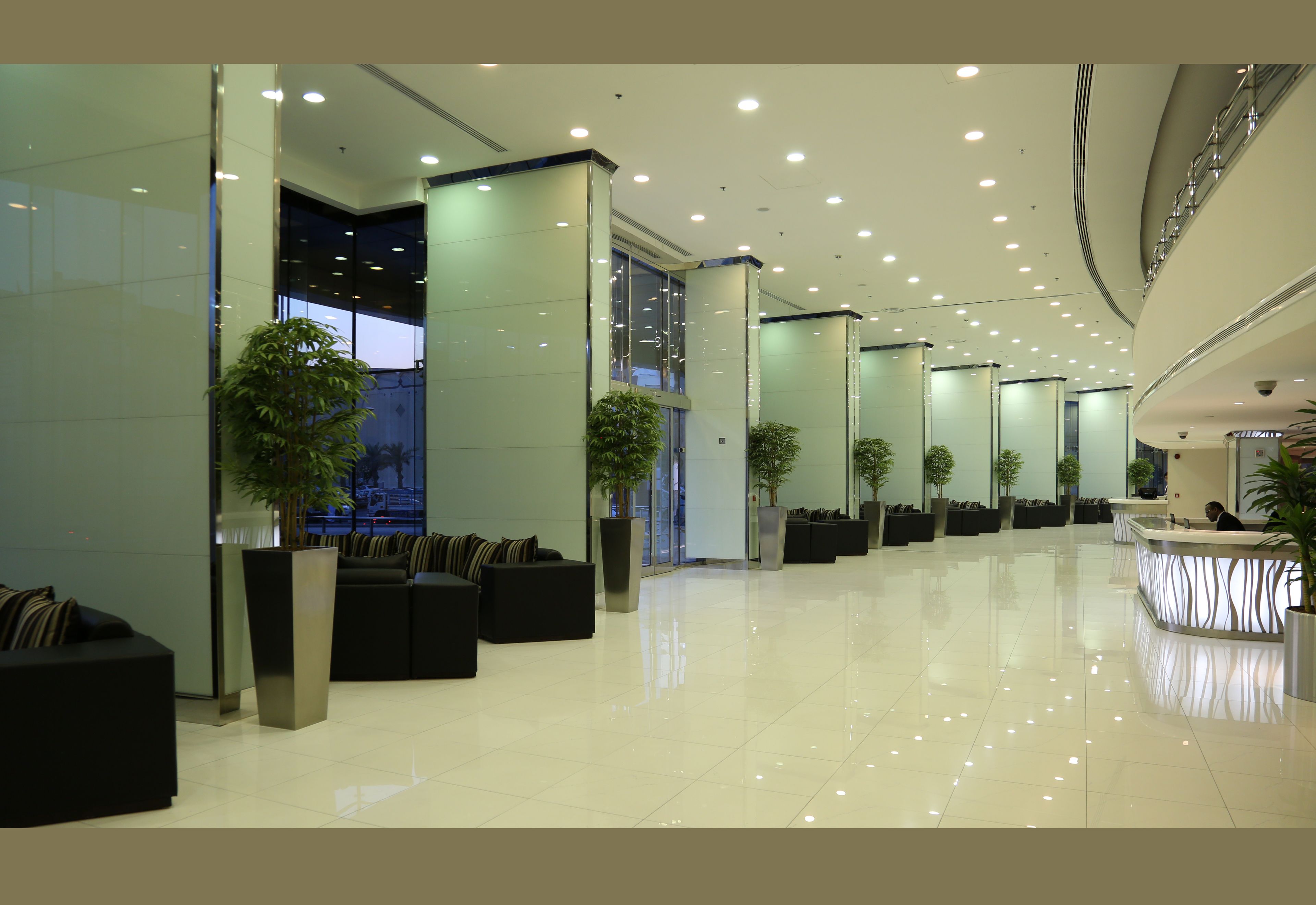 A modern lobby with a reception desk, seating areas, and potted plants.