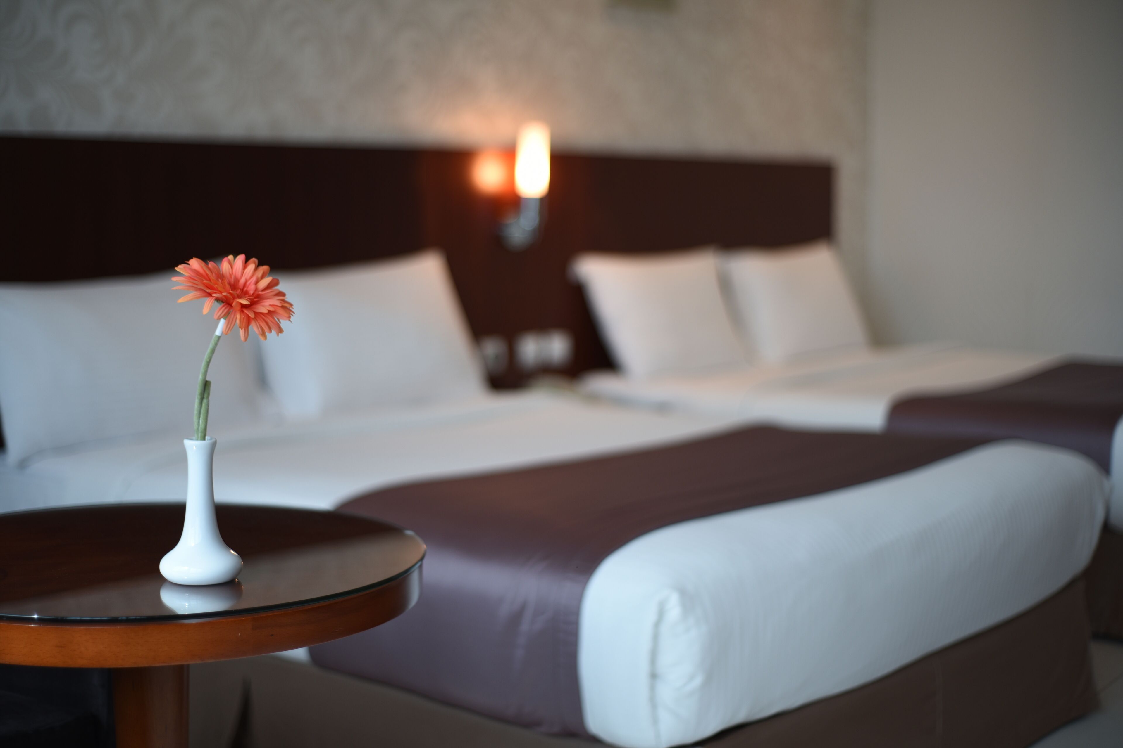 A hotel room with a bed, a nightstand, and a vase with a flower on a small table.