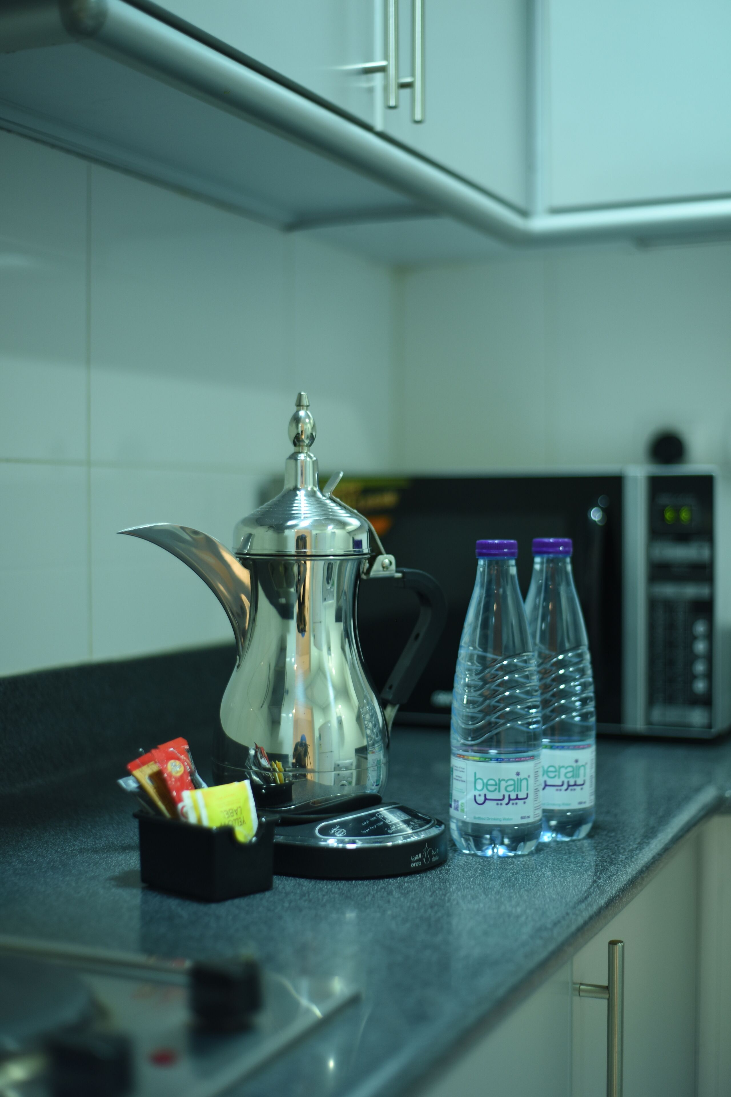 Una encimera de cocina con un hervidor plateado, dos botellas de agua y una cafetera negra.