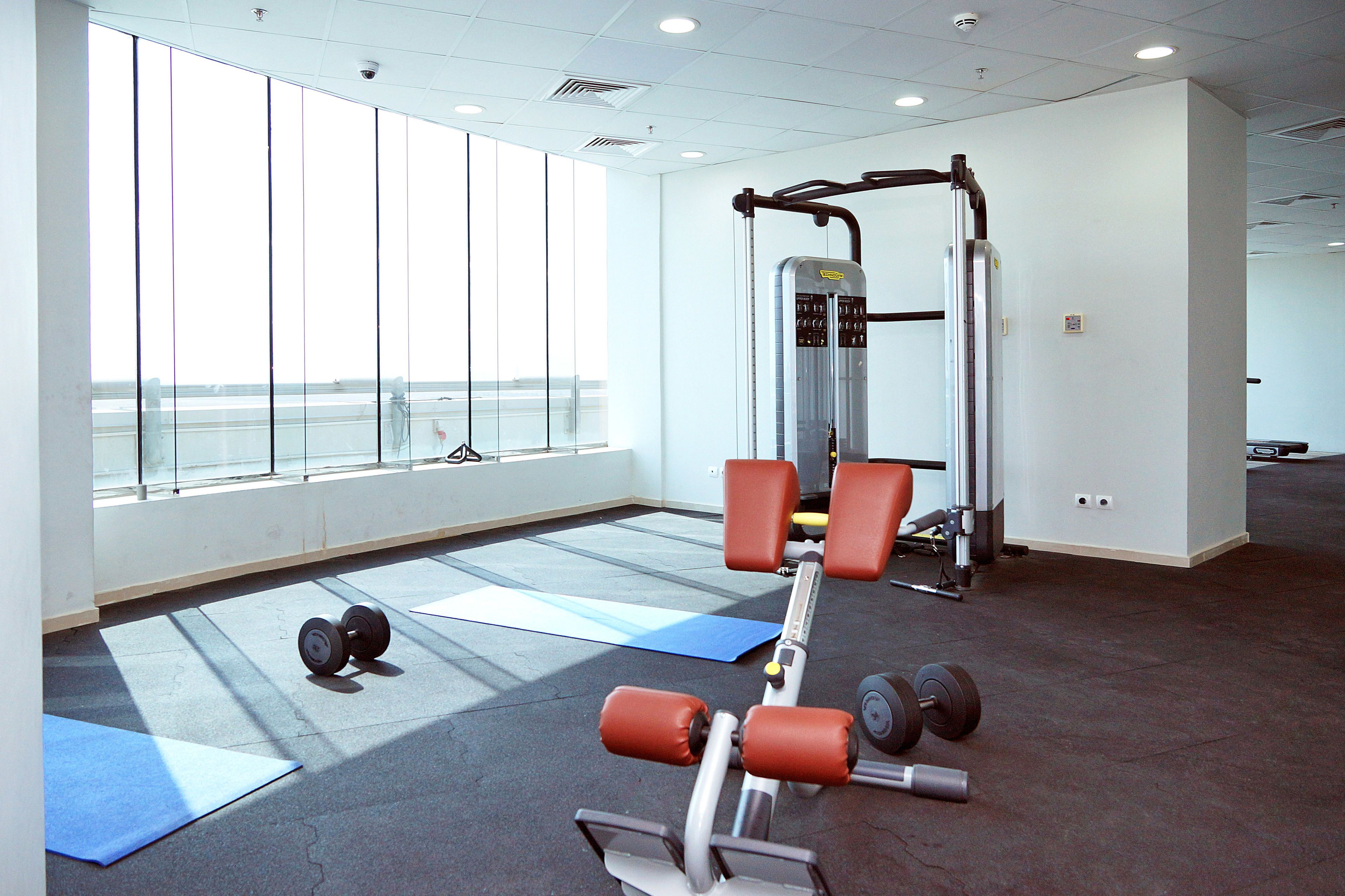 Un gimnasio con equipamiento de ejercicio, colchonetas y amplias ventanas.
