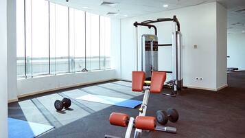 Un gimnasio con equipamiento de ejercicio, colchonetas y amplias ventanas.