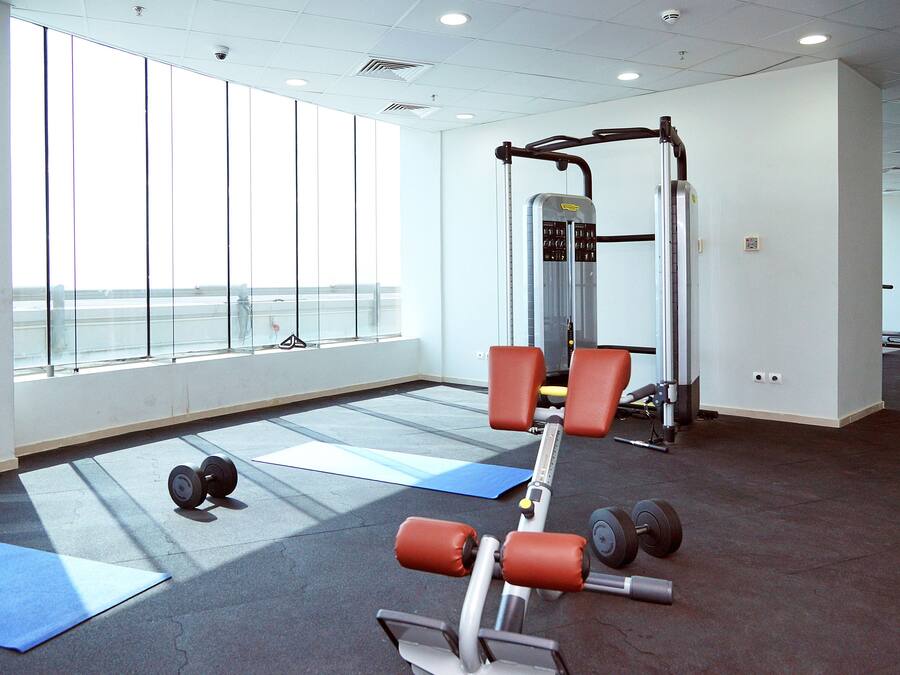 Un gimnasio con equipamiento de ejercicio, colchonetas y amplias ventanas.