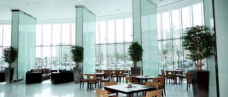 A spacious indoor area with large windows, modern furniture, and potted plants.