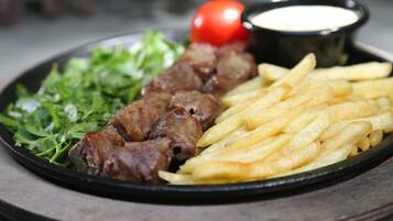 A plate with kebabs, fries, a tomato, and a small bowl of sauce.
