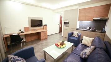 A modern living room with a sofa, coffee table, and a TV. There is a kitchen area with cabinets and appliances.
