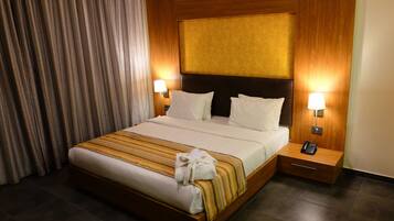 Habitación de hotel con una cama grande, dos lámparas de noche, un cabecero de madera y suelo oscuro.