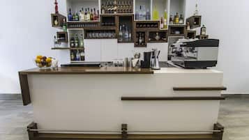 Een bar met een wit aanrecht, houten planken met flessen en een koffieapparaat.