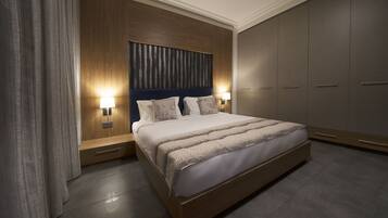 A modern bedroom with a large bed, wooden headboard, bedside lamps, and a wardrobe.