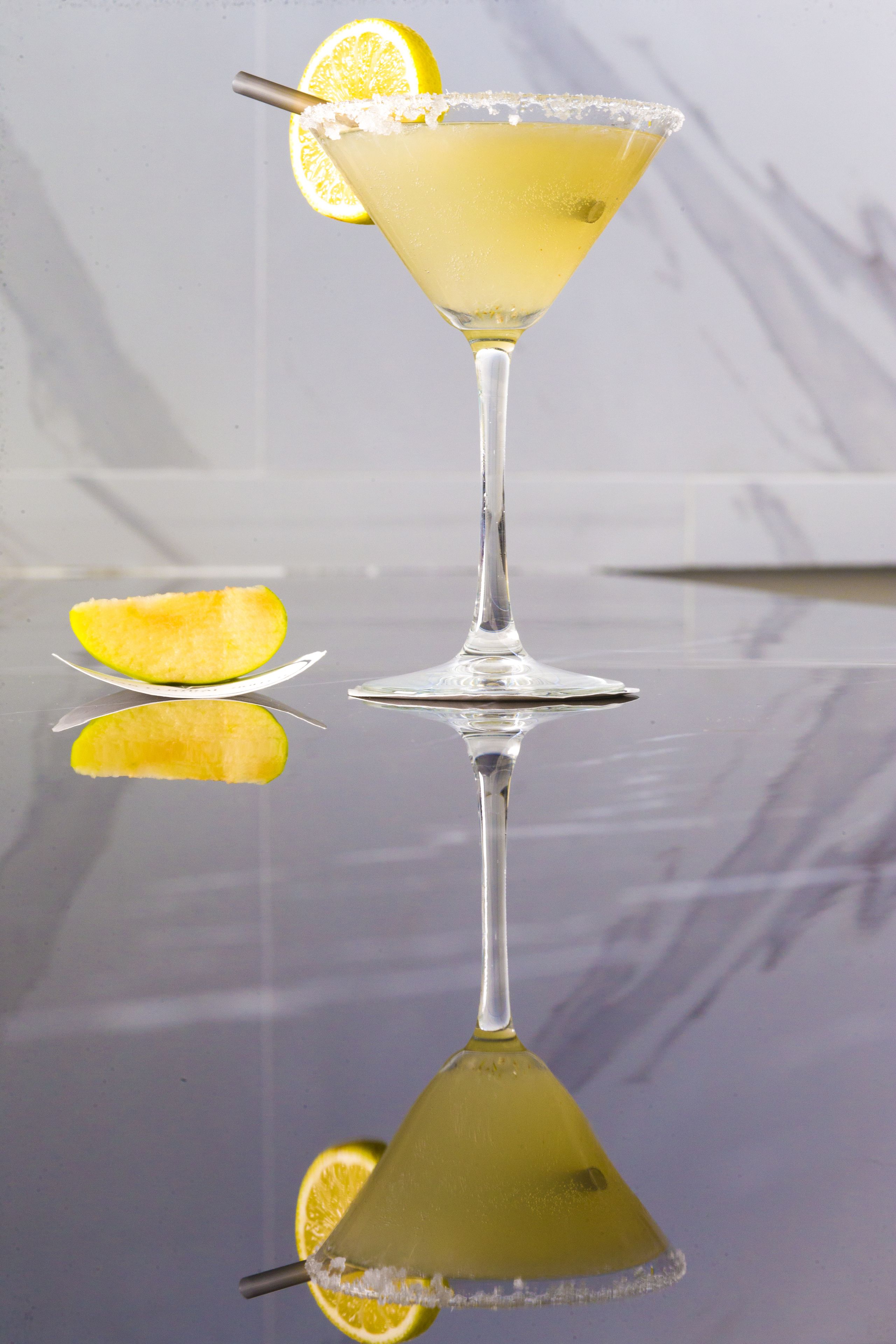 Un verre à martini, orné d’une tranche de citron, posé sur une surface réfléchissante.