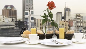 Desayuno con cruasanes, jugo y una rosa en un balcón con vista a la ciudad.