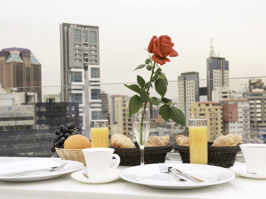 Desayuno con cruasanes, jugo y una rosa en un balcón con vista a la ciudad.