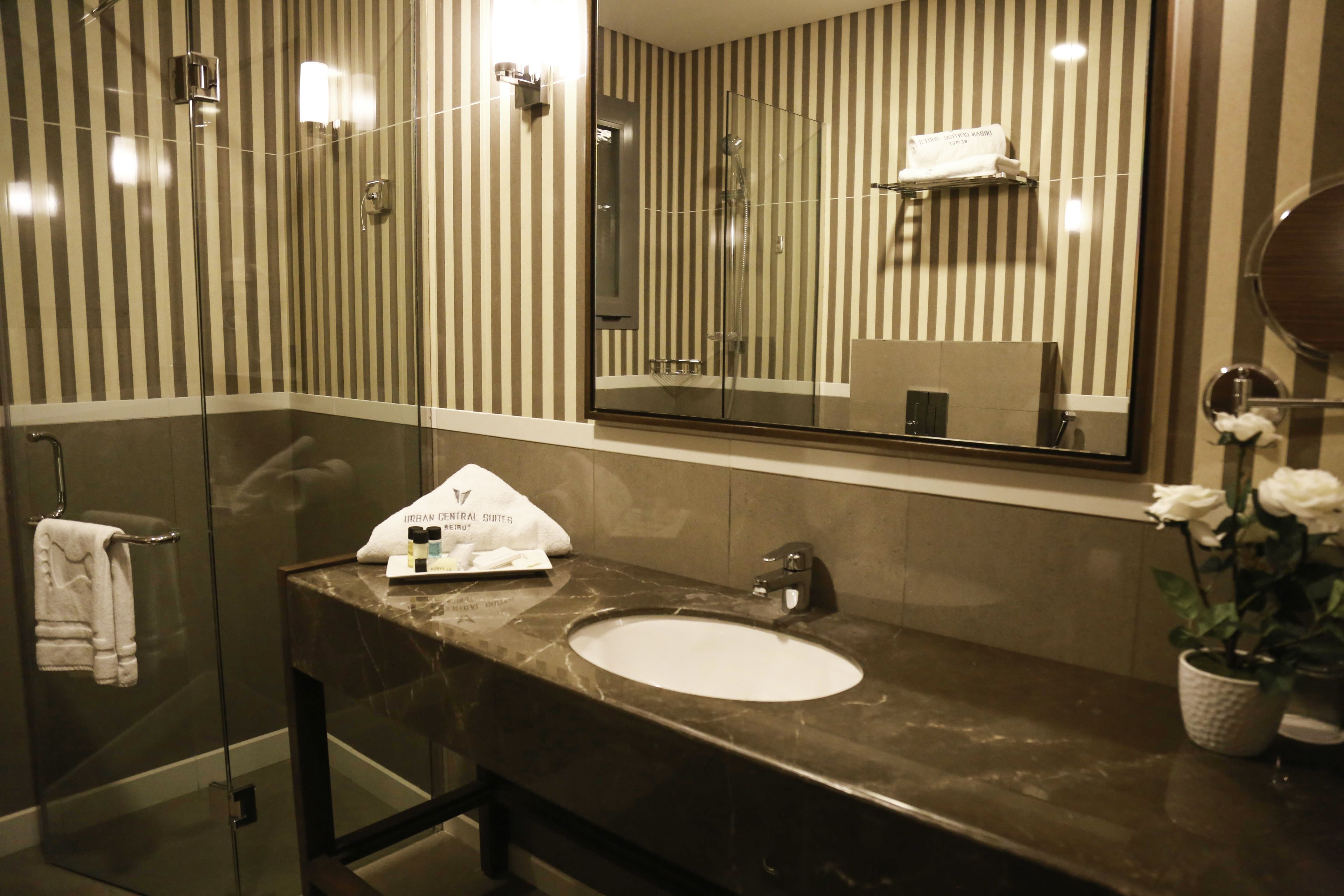 Un baño con cabina de ducha de vidrio, lavamanos de mármol y un espejo grande.