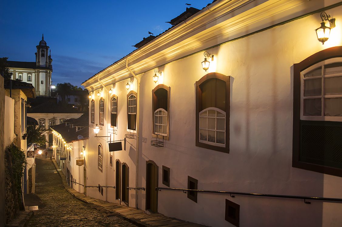 A narrow cobblestone street lined with historic buildings, featuring arched windows and traditional lighting fixtures.