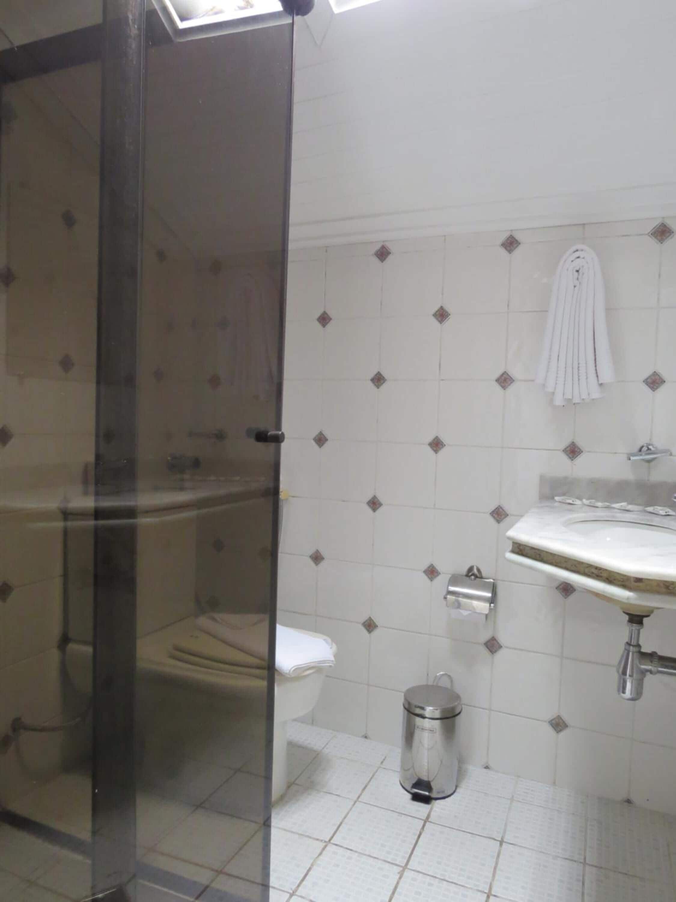 A bathroom with a glass shower enclosure, a toilet, a sink with a marble countertop, and a towel hanging on the wall.