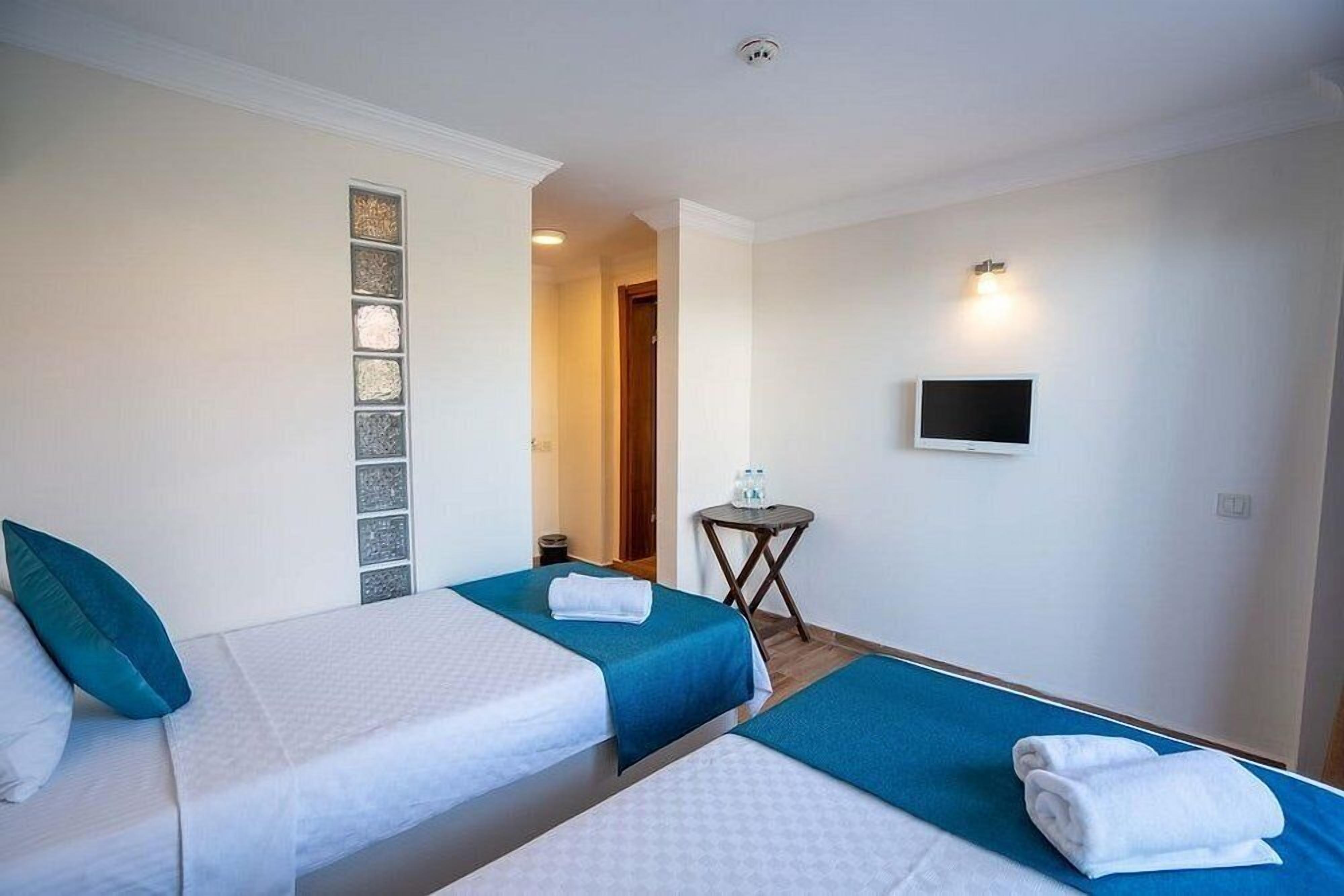 A hotel room with two beds, a small table with a water bottle, a TV on the wall, and a decorative wall panel.