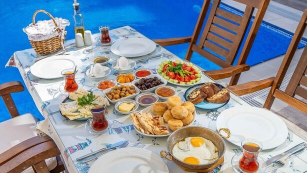 A table set with a variety of dishes, including eggs, bread, olives, and salads, by a poolside. - Cunda Giritlioğlu Otel (Ayvalik)