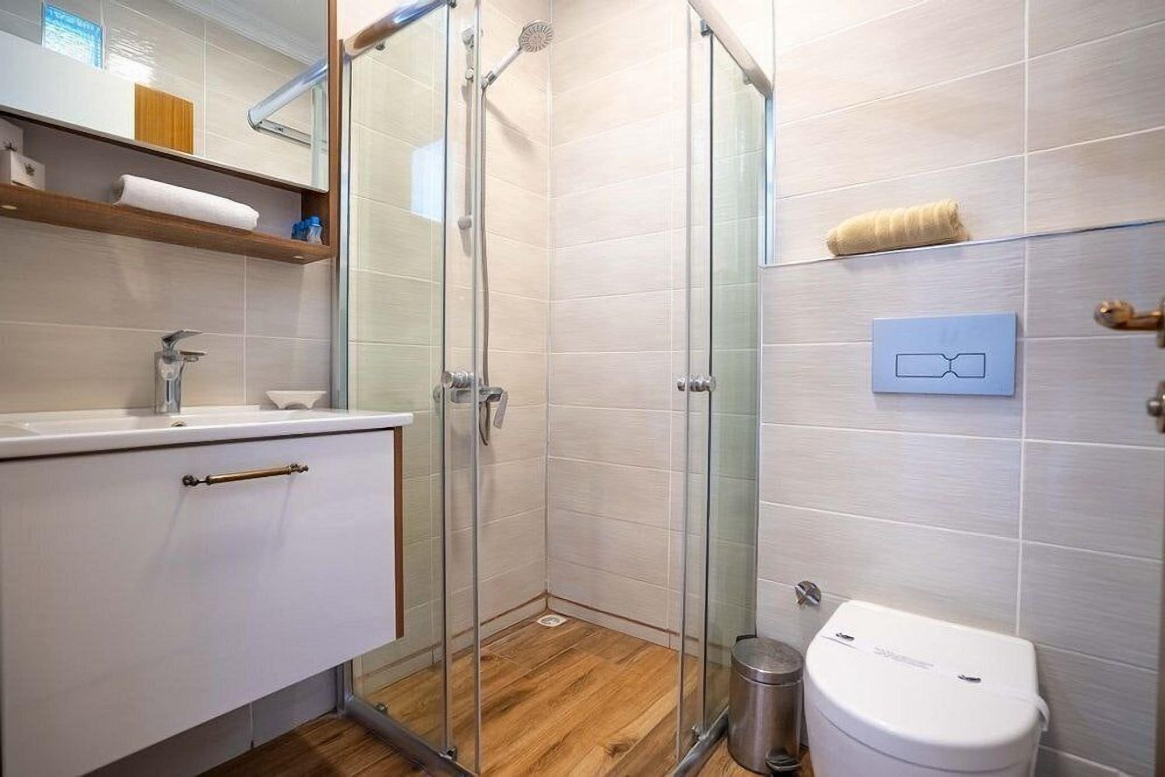 Ein modernes Badezimmer mit einer Duschkabine aus Glas, einer weißen Toilette und einem hölzernen Waschtisch mit Handtuchablage.