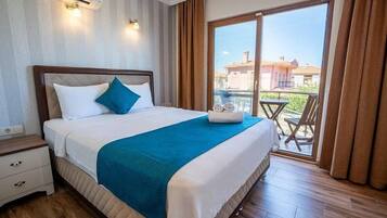 Habitación de hotel con cama, mesita de noche, una mesa con sillas afuera y vista a edificios.