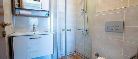 A bathroom with a glass shower enclosure, a white sink, and a toilet.