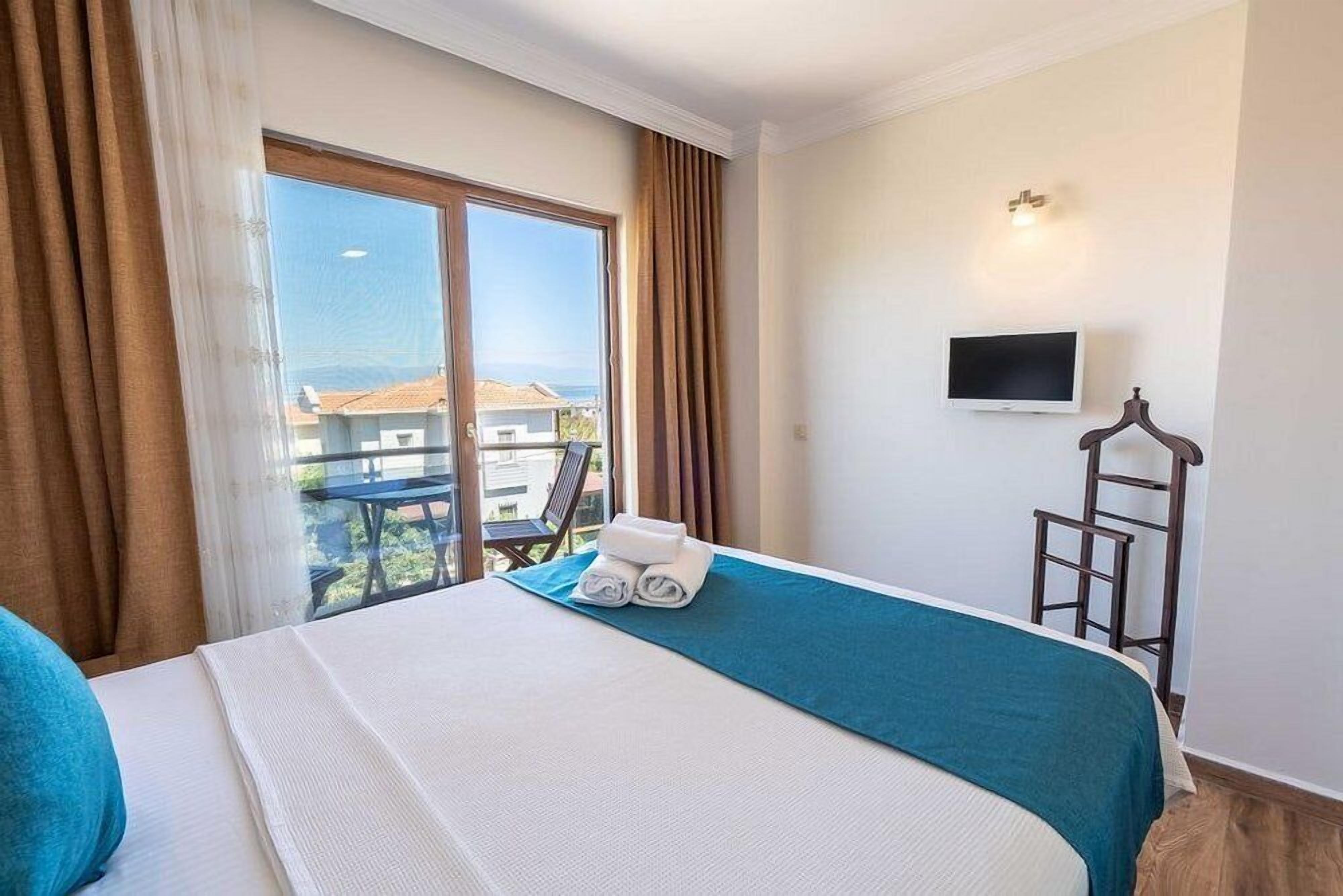A hotel room with a bed, a TV, a balcony with a view, and a chair.