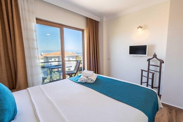 A hotel room with a bed, a TV, a balcony with a view, and a chair.