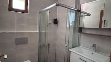 Un baño con cabina de ducha de vidrio, inodoro, lavamanos y espejo.