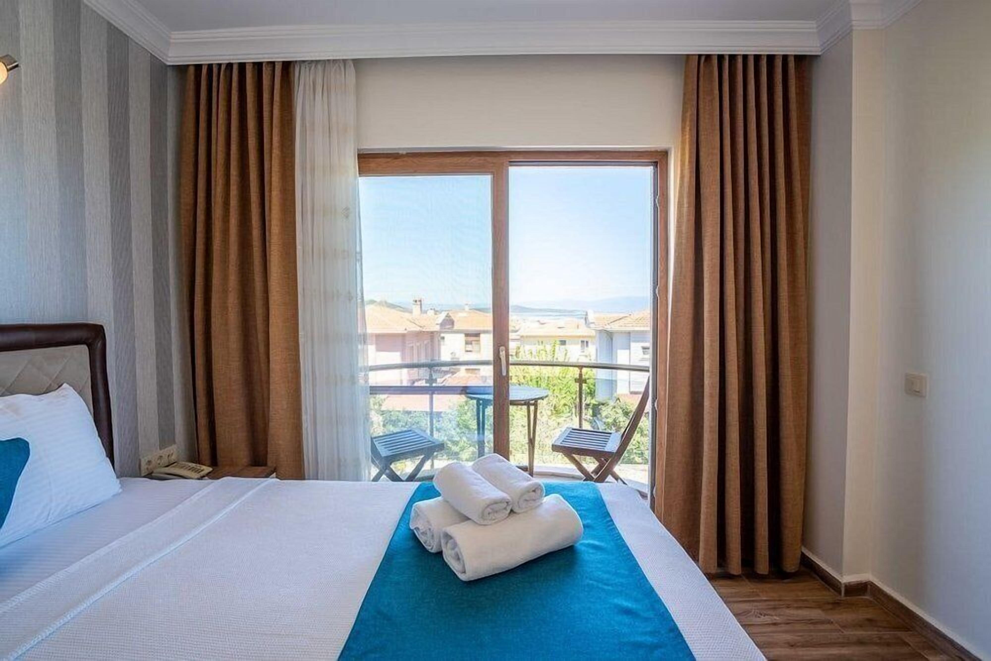 A hotel room with a bed, a view of the beach, and a balcony with chairs.