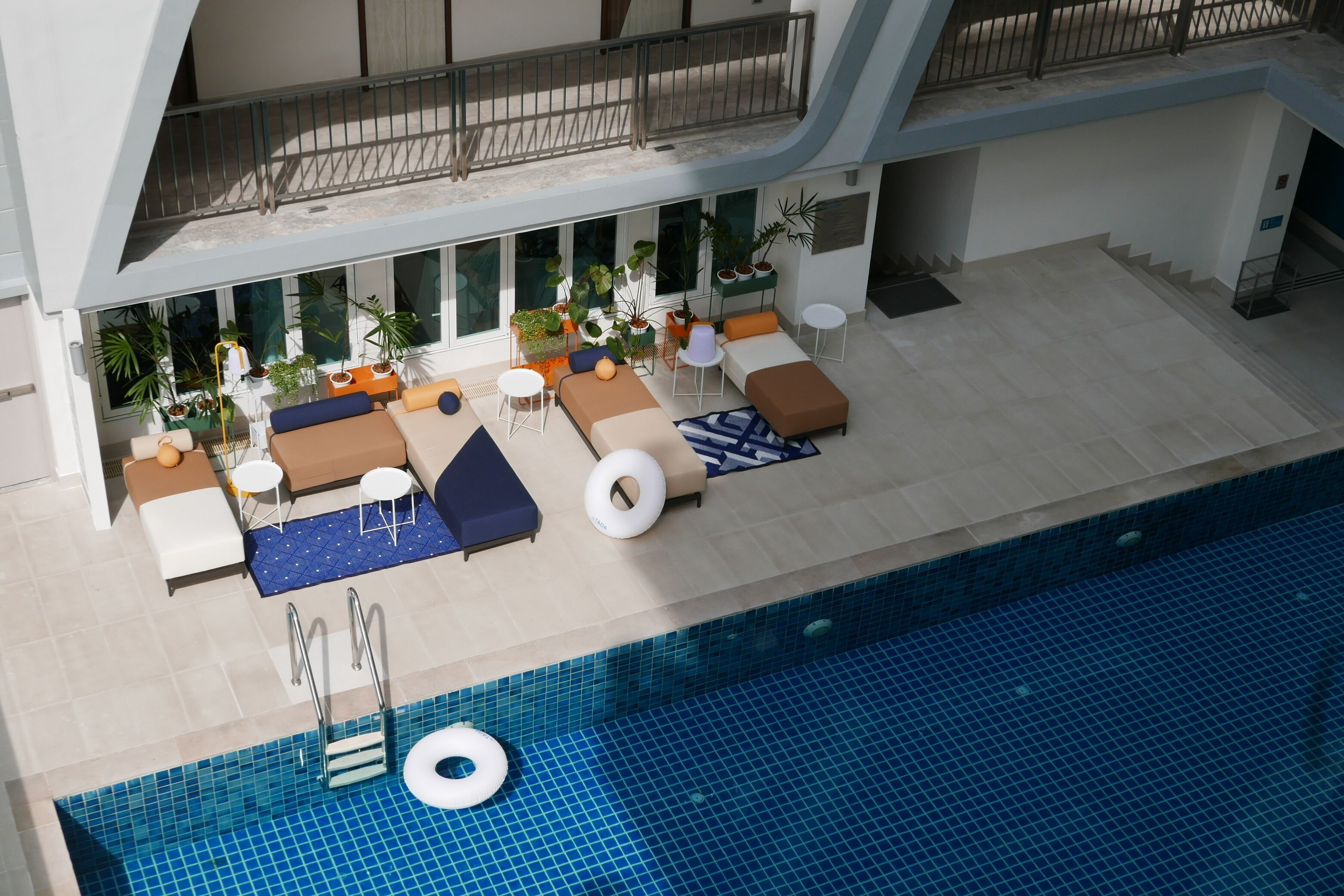 A modern indoor pool area with lounge seating, a floating ring, and potted plants.
