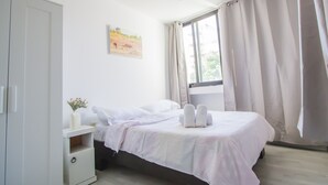 Un dormitorio con cama, mesita de noche, armario y ventana con cortinas.