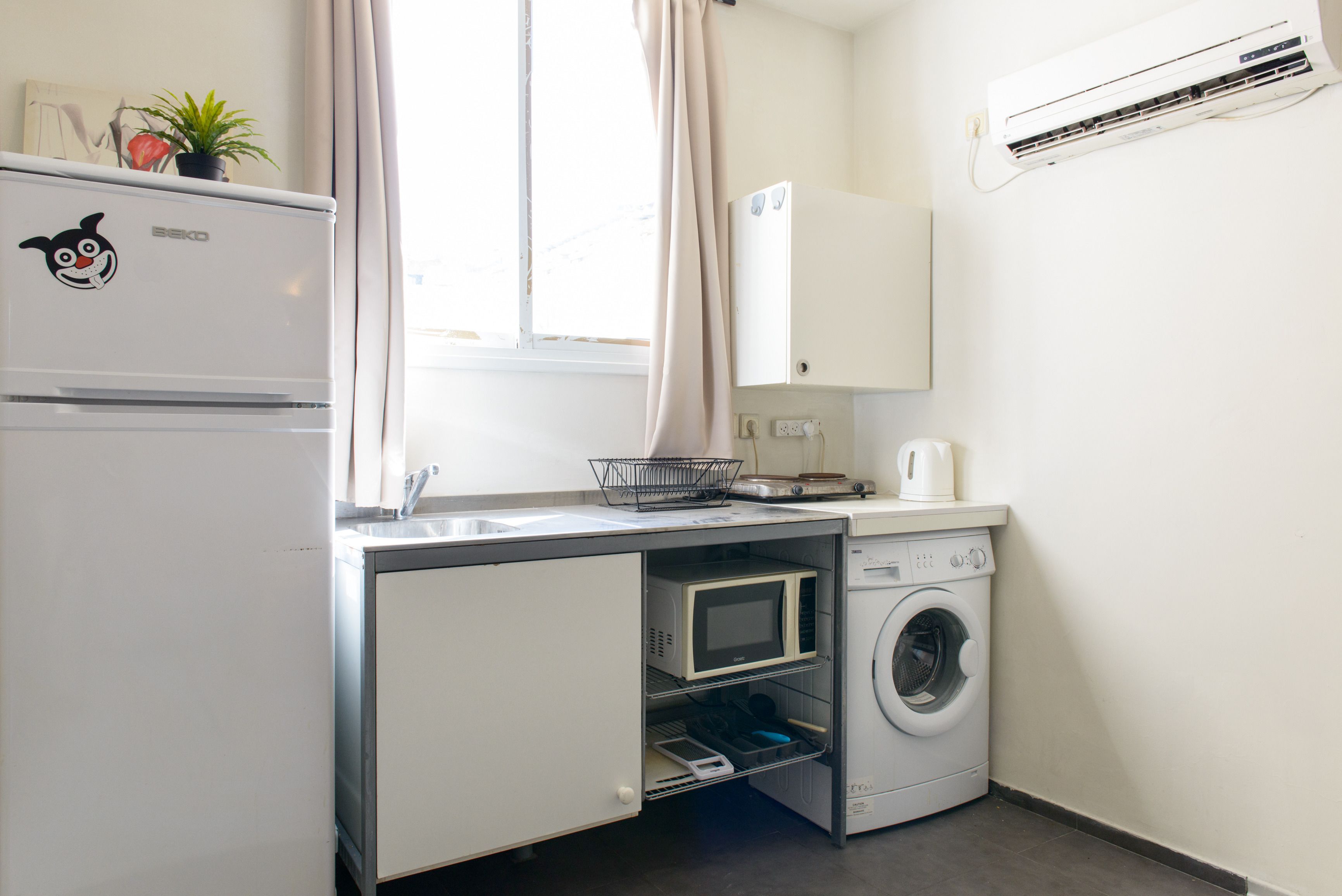 Una kitchenette compacta con refrigerador, microondas y lavadora.