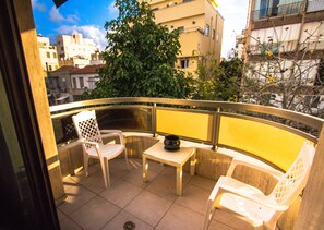 A balcony with a white plastic chair, a small table, and a potted plant.