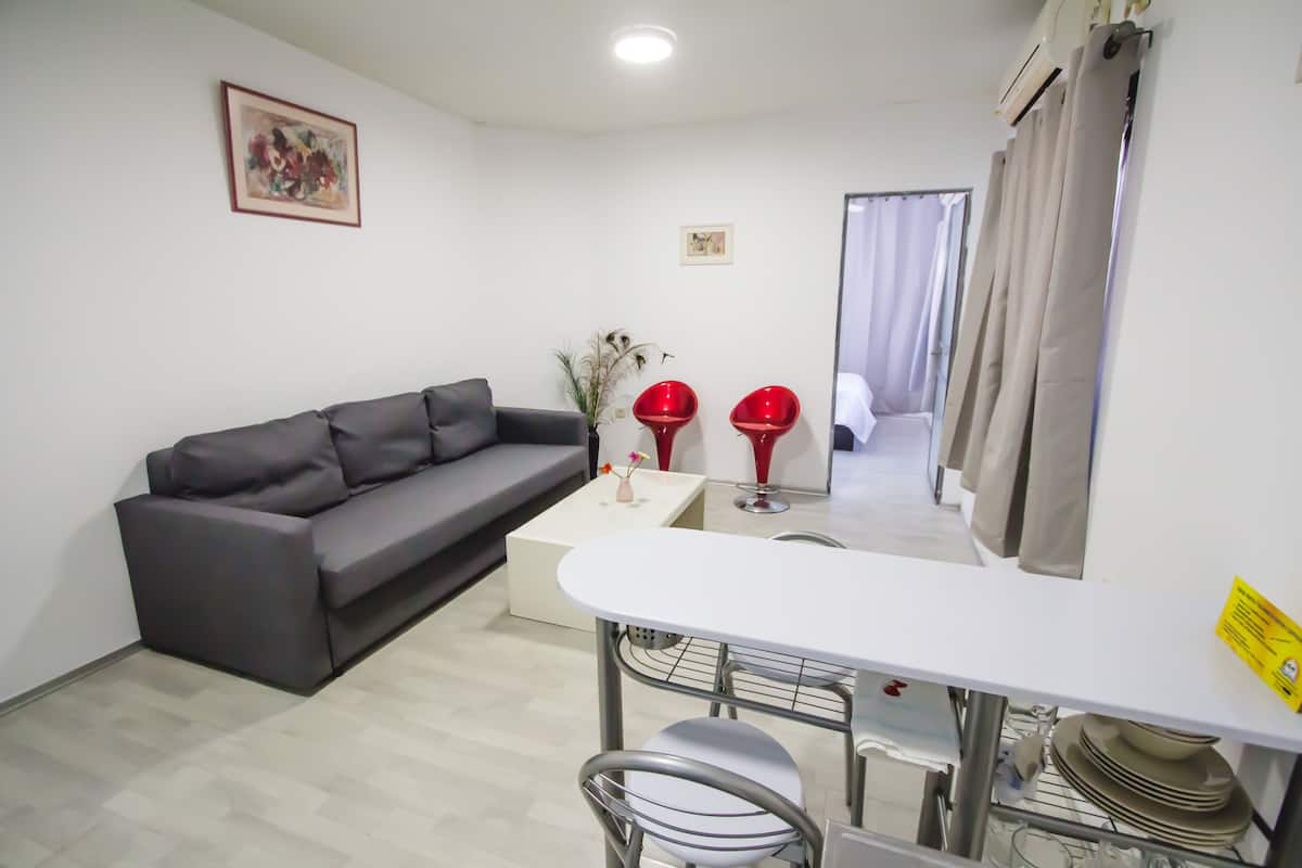 A modern living room with a grey sofa, a white coffee table, and a dining area with a white table and metal chairs.