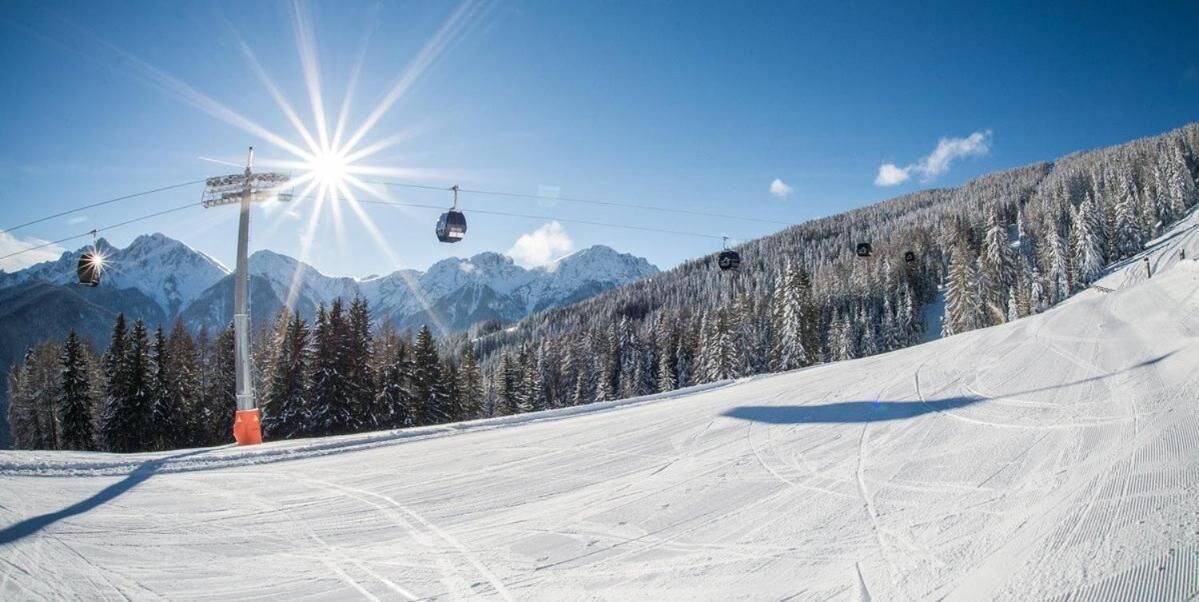 A ski slope with a ski lift, snow-covered trees, and mountains in the background.