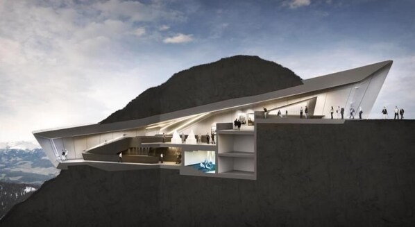 Un edificio moderno dal design architettonico con tetto spiovente e più livelli, immerso in un paesaggio montuoso.