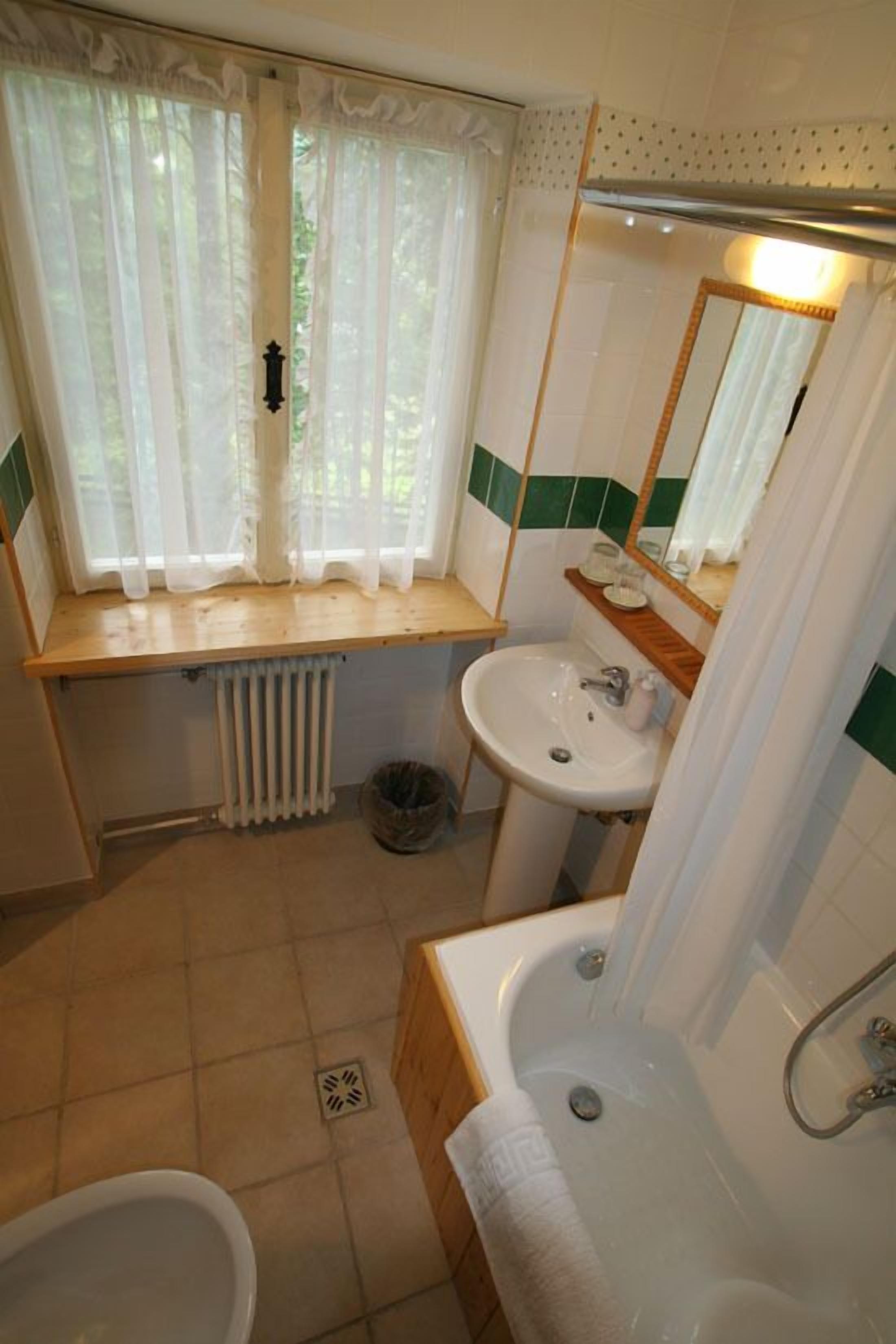 Ein kleines Badezimmer mit Fenster, Waschbecken, Badewanne und Toilette.