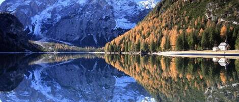 A serene mountain lake with a clear reflection of the surrounding landscape, including a church and forested area.