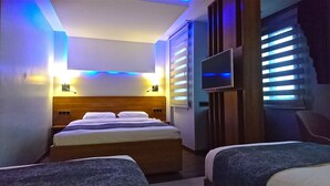 A hotel room with a bed, a TV mounted on the wall, and a window with blinds. - Nur Hotel (Trabzon)