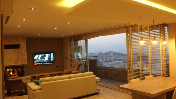A modern living room with a fireplace, a sofa, a TV, and a dining area with a view of the city. - Nur Hotel (Trabzon)
