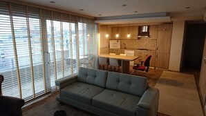 A modern living room with a sofa, a dining table with chairs, and a kitchen area with wooden cabinets and a stove. - Nur Hotel (Trabzon)