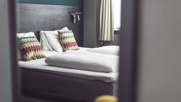 A neatly made bed with white linens and two colorful pillows, a gray headboard, and a window with curtains.