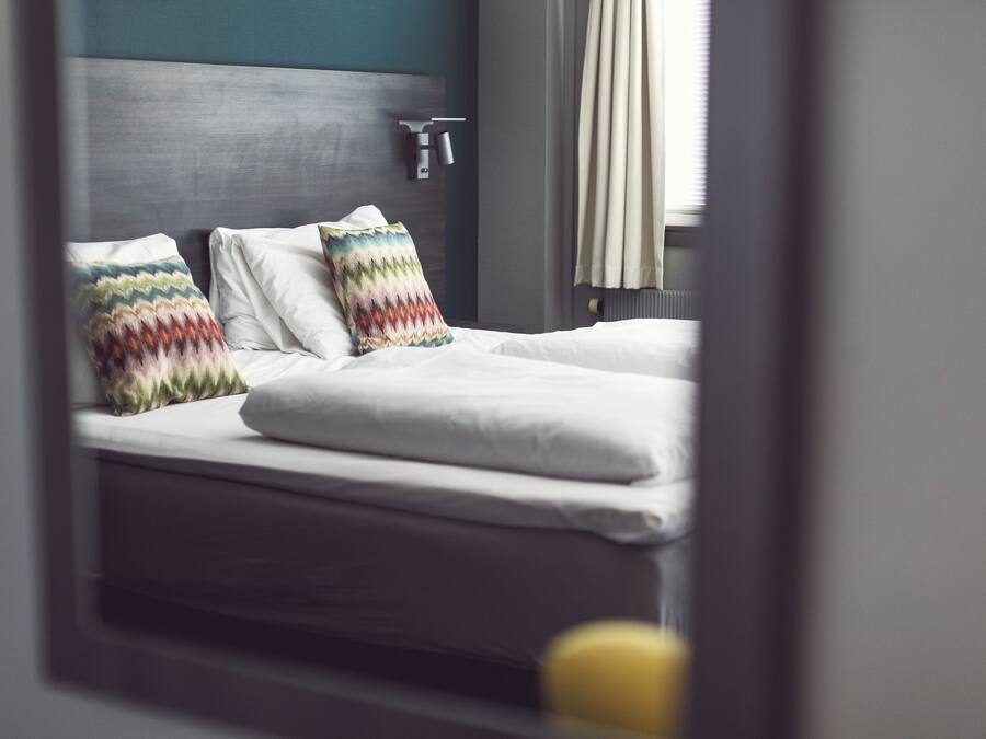 A neatly made bed with white linens and two colorful pillows, a gray headboard, and a window with curtains.