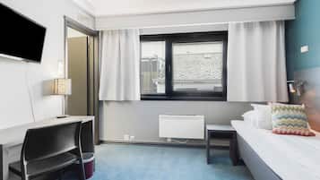 Una habitación de hotel con cama, escritorio, silla, televisor, ventana con cortinas y radiador.