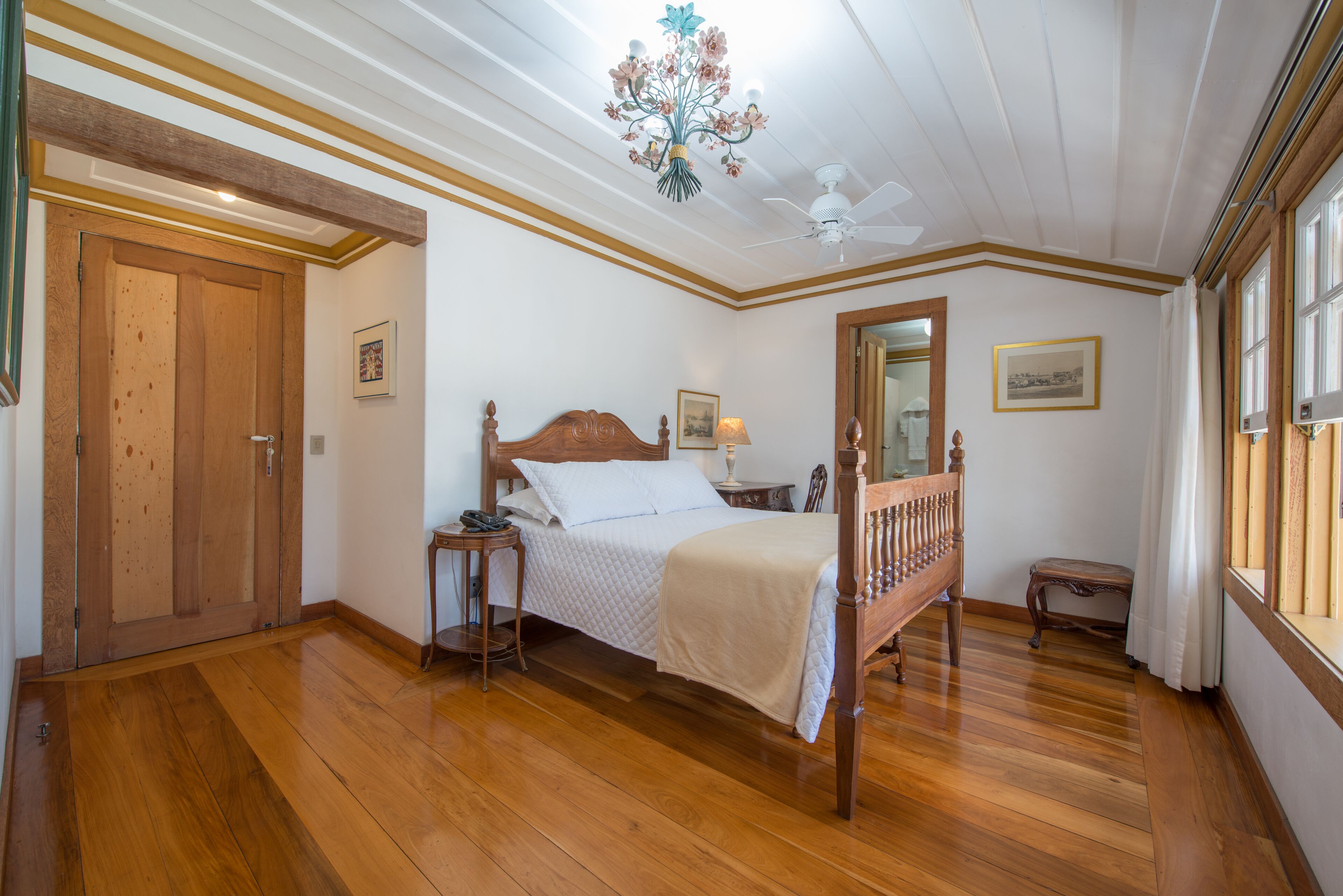Una camera da letto con un letto in legno, un comodino, una sedia, un ventilatore a soffitto e un'ampia finestra.
