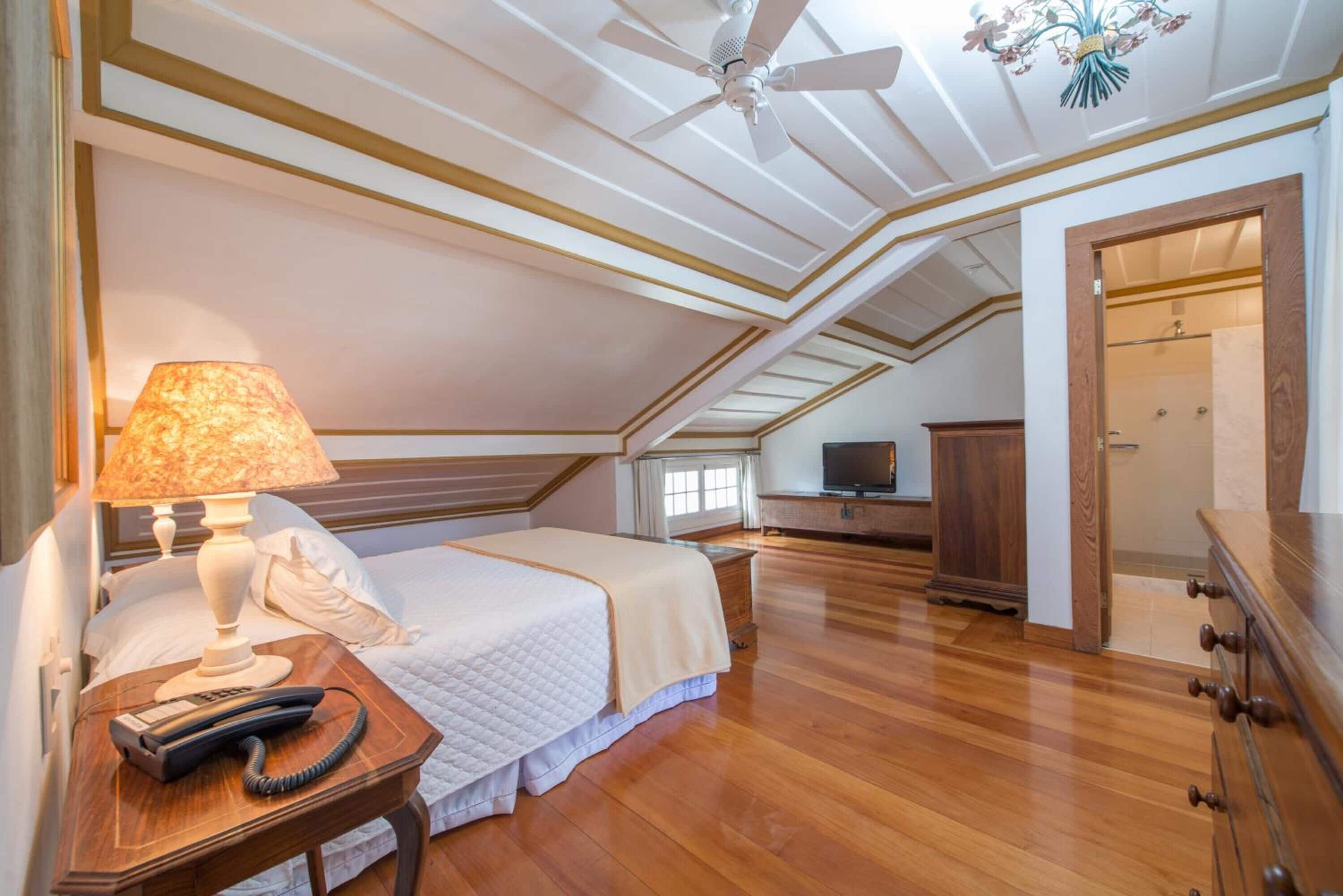 A bedroom with a bed, a bedside lamp, a telephone, a television, and a wooden dresser.