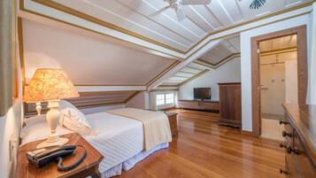 A bedroom with a bed, a bedside lamp, a telephone, a television, and a wooden dresser.