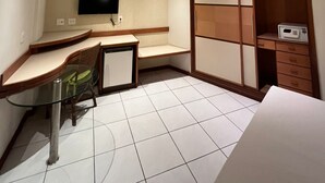 Une chambre d’hôtel moderne dotée d’un bureau incurvé, d’un téléviseur à écran plat fixé au mur, d’un dressing avec des portes en bois et d’un four à micro-ondes posé sur un meuble.